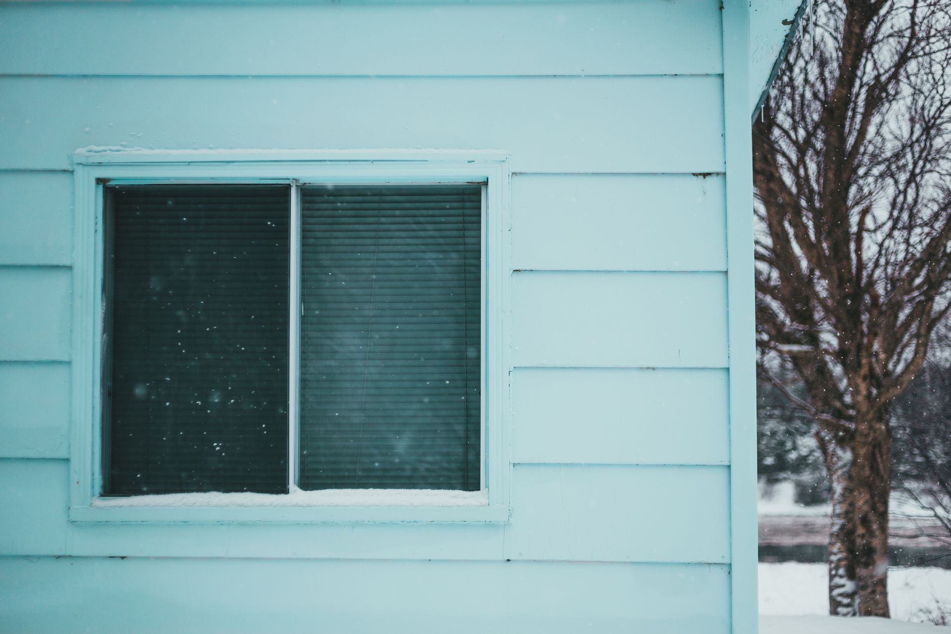 Exterior of wooden house corner with mint walls and square window with closed blinds in blizzard weather in in Austin, TX