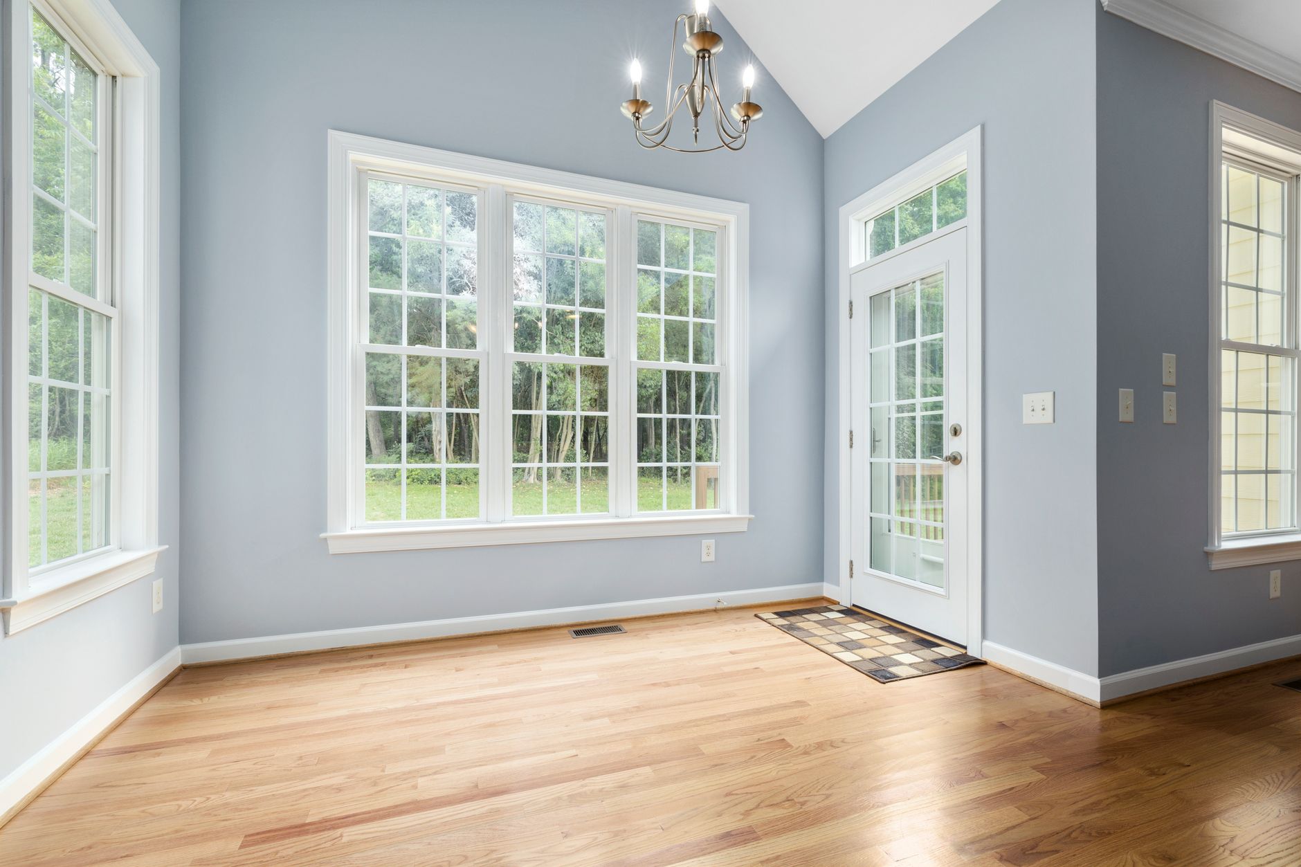 Sunlit empty room with wooden floor, chandelier, and French windows leading outside in Austin, TX