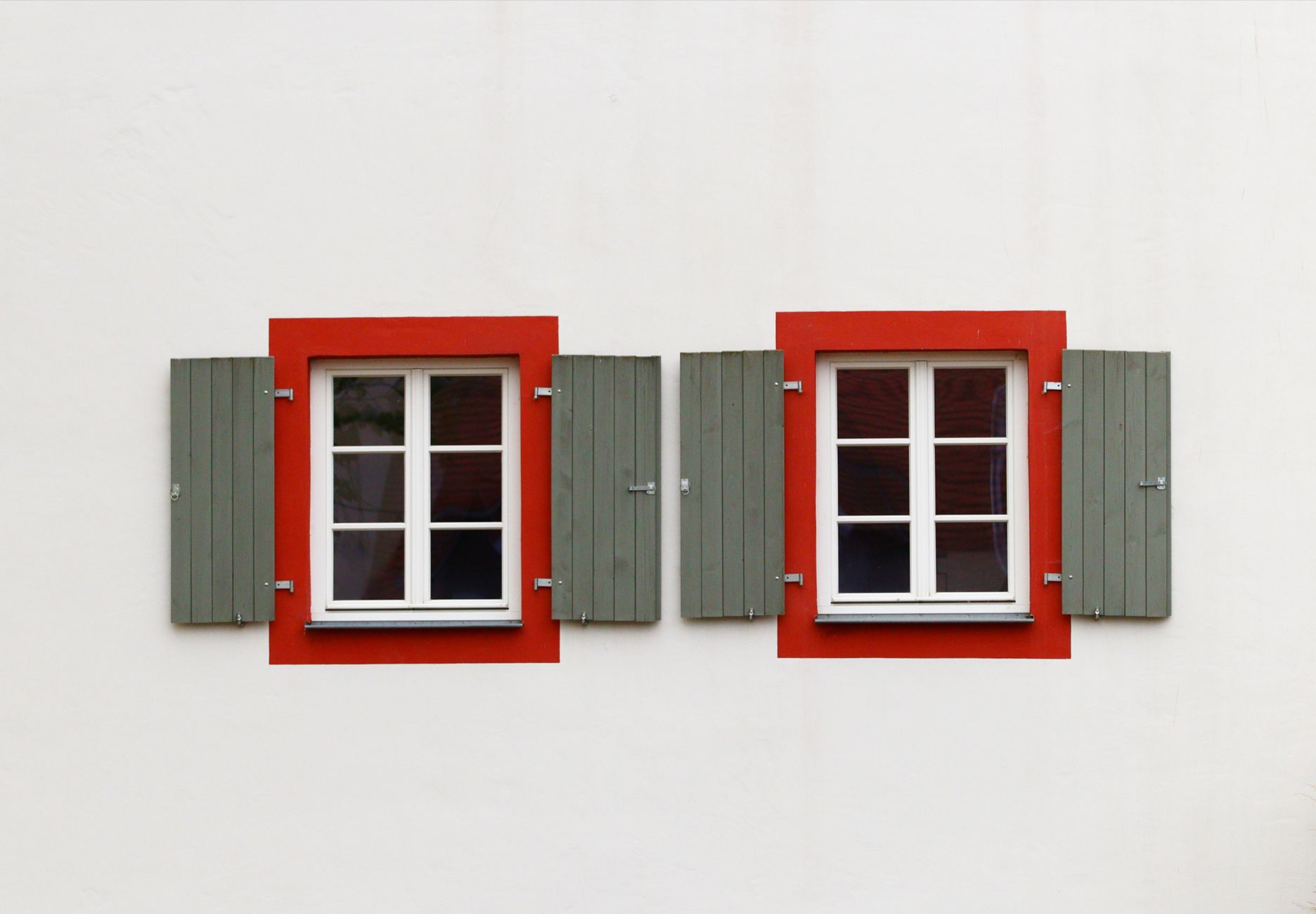 Symmetrical windows with red frames and green shutters on a white wall, minimalist design in Austin, TX
